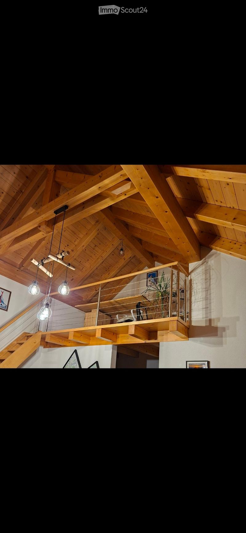 Open wooden ceiling with exposed beams and pendant lights, overlooking a balcony area with a railing and potted plants.