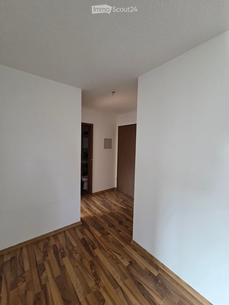 Empty hallway with wooden flooring and white walls, featuring two doors leading to other rooms.