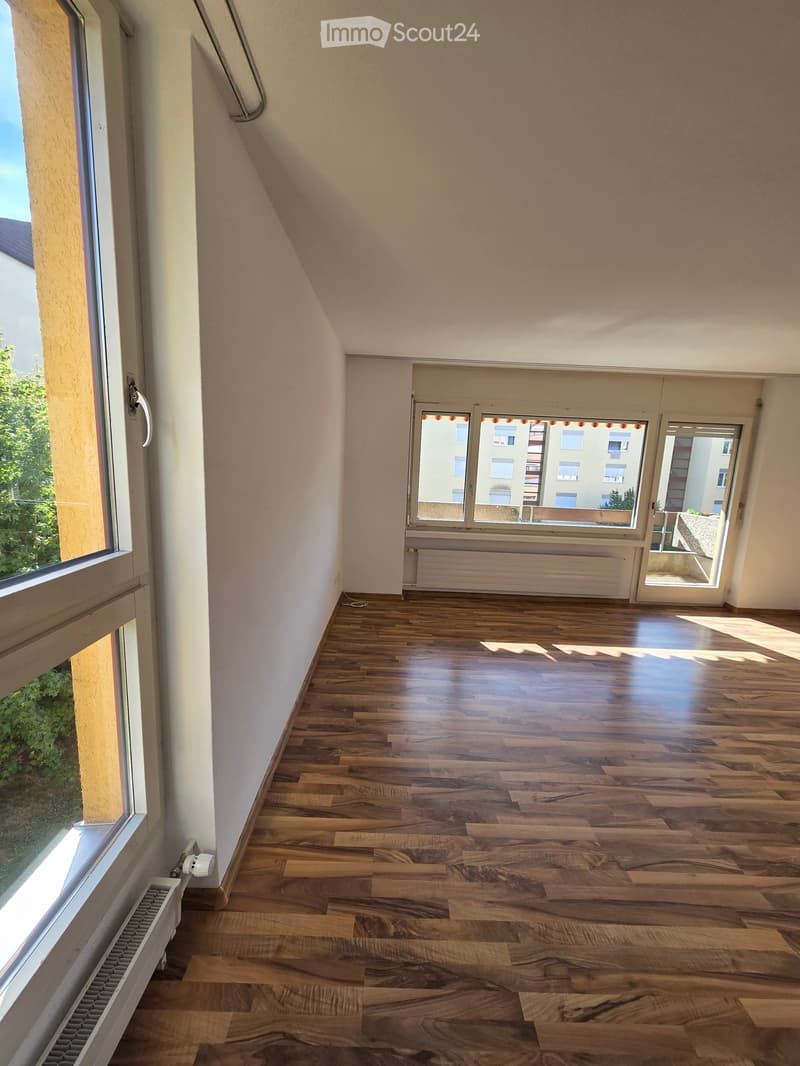 Empty hallway with wooden flooring, white walls, large windows, and radiators visible on both sides.