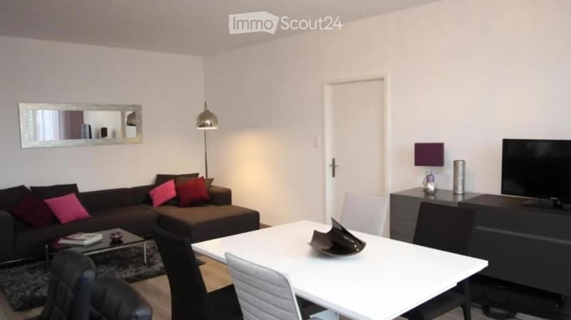 Modern living room with a dark brown sofa, colorful cushions, a white coffee table, a dining table with chairs, a floor lamp, a wall-mounted mirror, and a TV stand with a television.