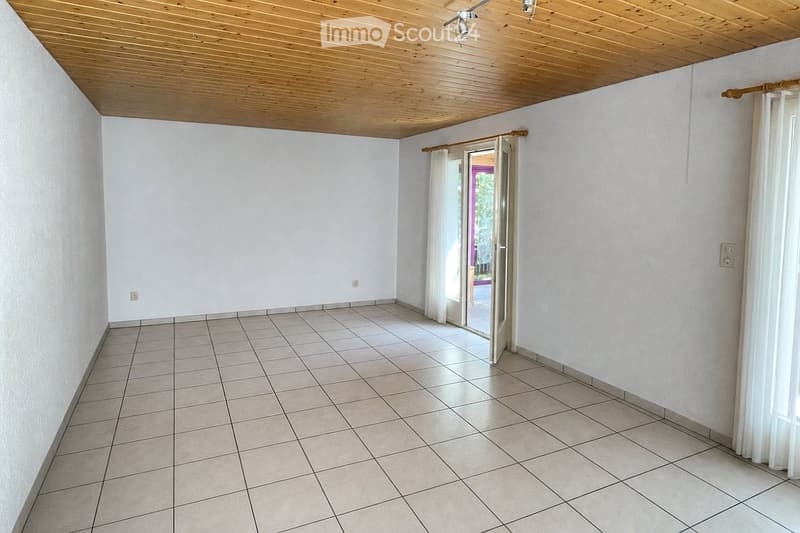 Empty room with tiled floor, white walls, wooden ceiling, and a sliding glass door leading outside.