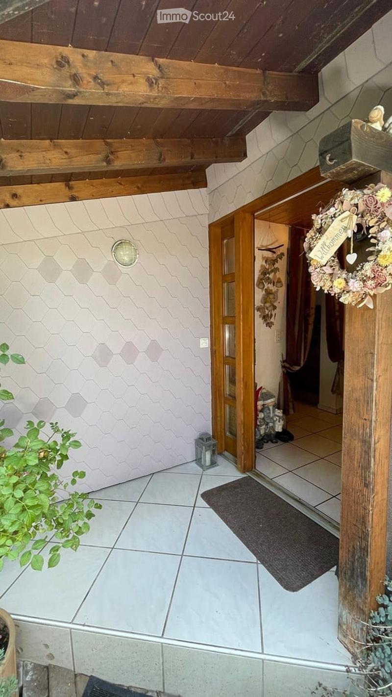 Entrance hallway with tiled flooring, wooden ceiling beams, and a decorative wreath on the wall. A small lantern and potted plant are visible.