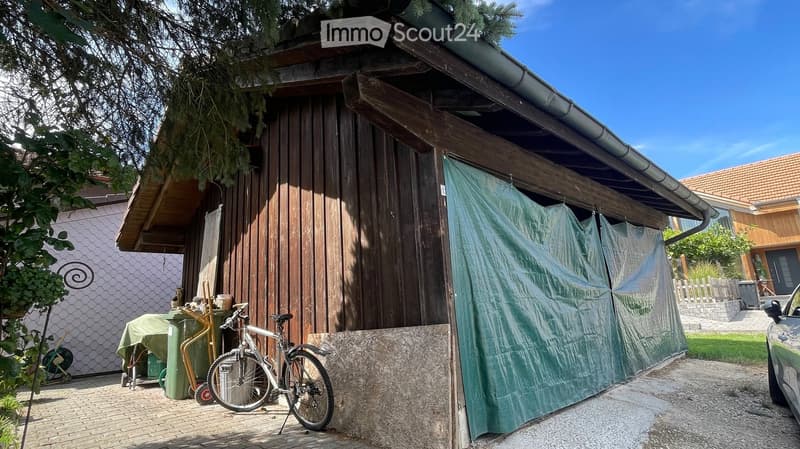 A wooden shed with a covered entrance, a bicycle parked nearby, and a green tarp covering part of the shed.