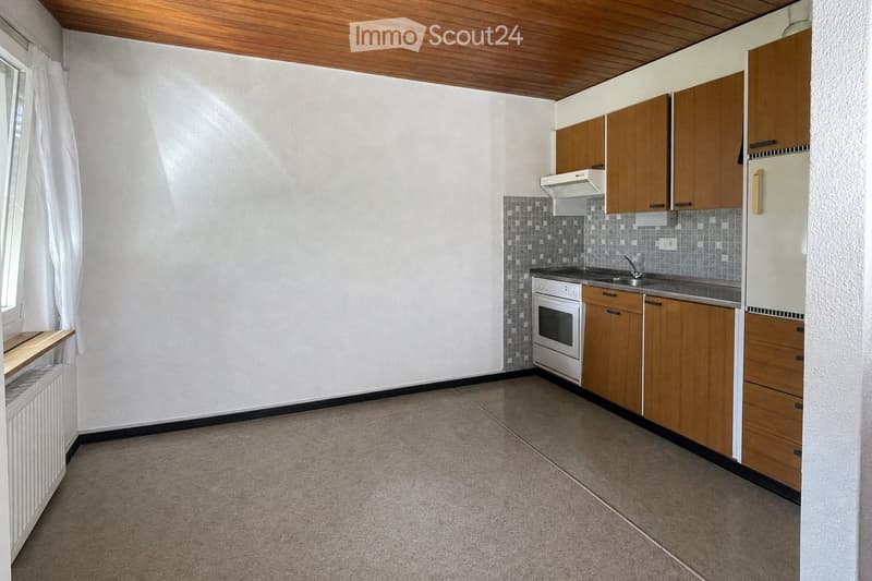 Empty kitchen with wooden cabinets, white oven, sink, and refrigerator. Light-colored walls and tiled backsplash.