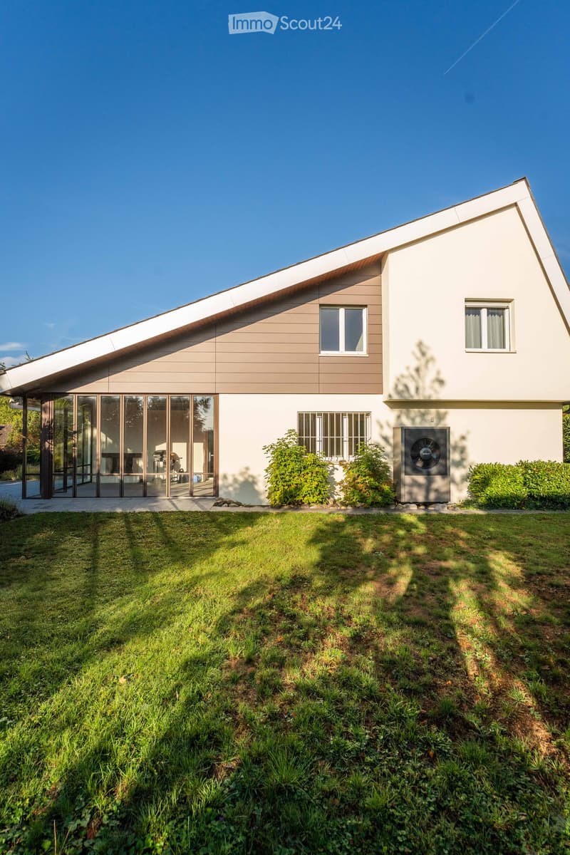 Modern two-story house with a flat roof, large glass sliding doors, and a well-maintained lawn.