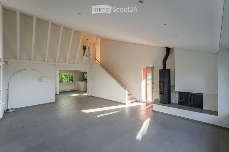 Open-plan living space with tiled floor, white walls, staircase leading to upper level, fireplace, and large window with view of greenery.