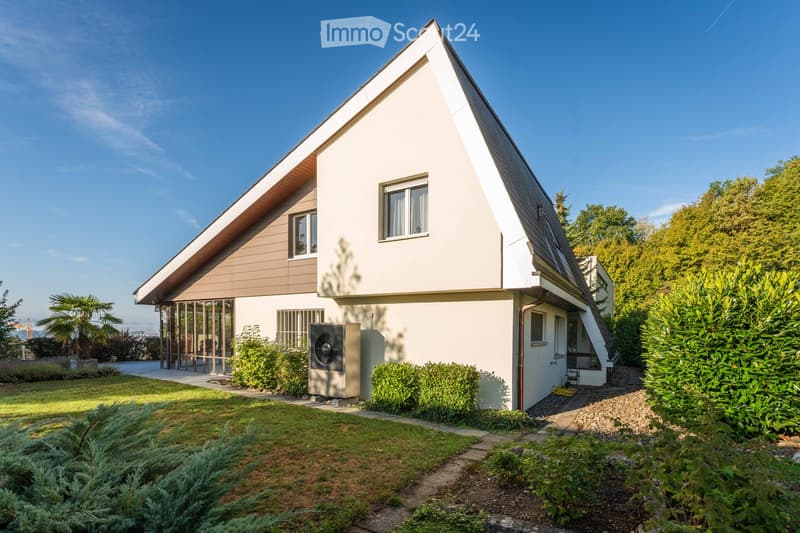 Modern single-family house with a flat roof and large windows, surrounded by a well-maintained garden with various shrubs and trees.
