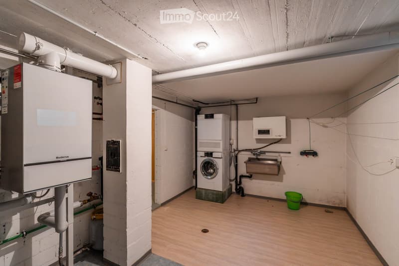 Utility room with a washing machine, water heater, control panel, sink, and visible pipes.