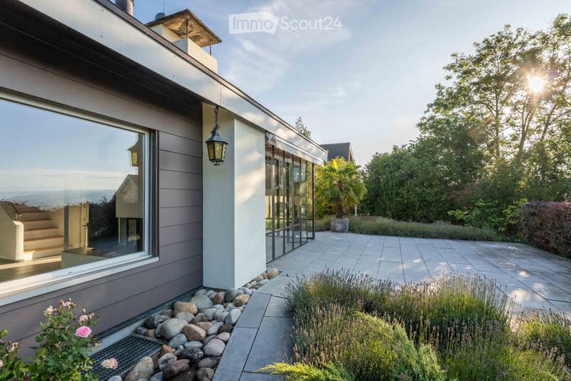 Modern house exterior with large windows, stone pathway, and landscaped garden featuring lavender and rocks.