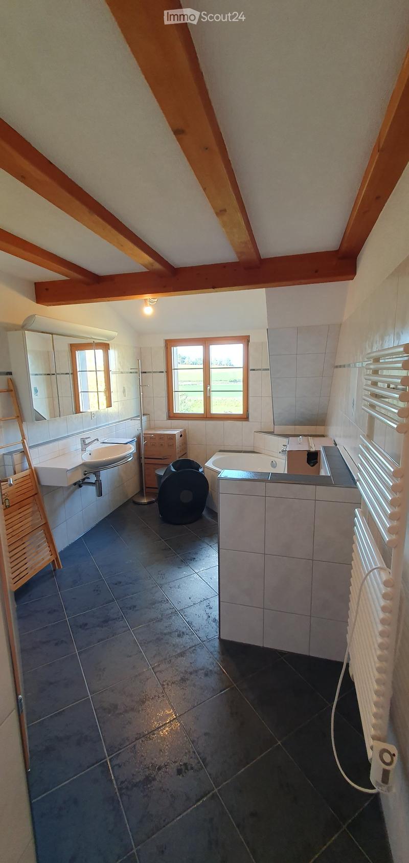 Bathroom with dark tiled floor, white tiled walls, sink, bathtub, mirror, radiator, and a wooden stool.