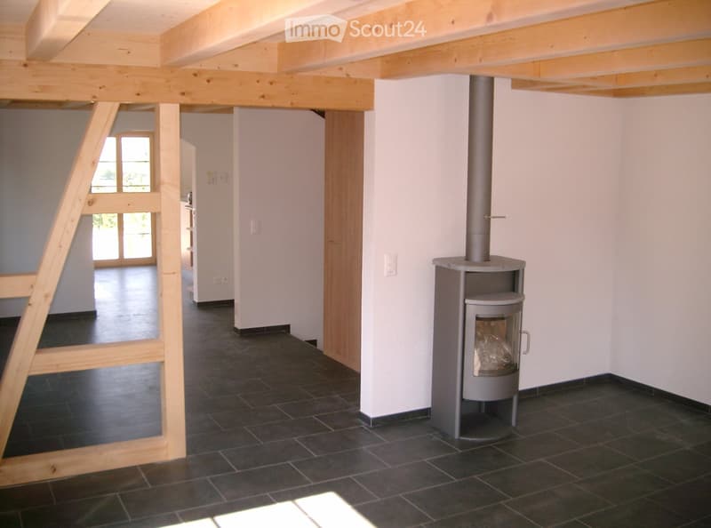 Unfurnished room with exposed wooden beams, dark tiled floor, and a modern wood-burning stove with a chimney.