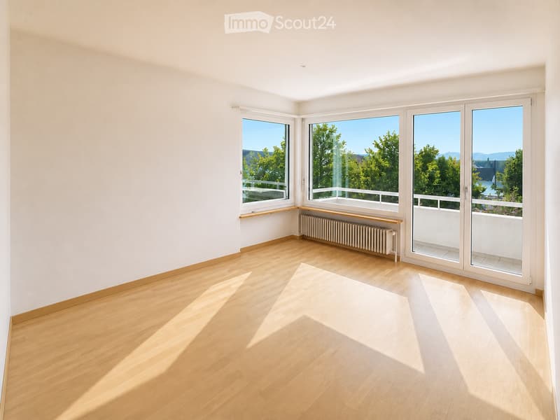 Empty room with wooden flooring, white walls, large windows, radiator, and a view of greenery and water.