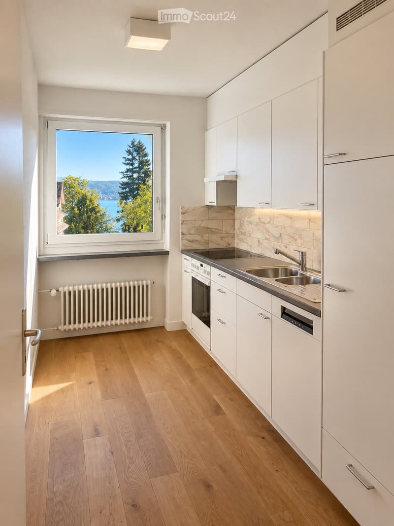 Modern kitchen with white cabinets, wooden flooring, a large window offering a scenic view, and stainless steel appliances including a sink, faucet, and oven.