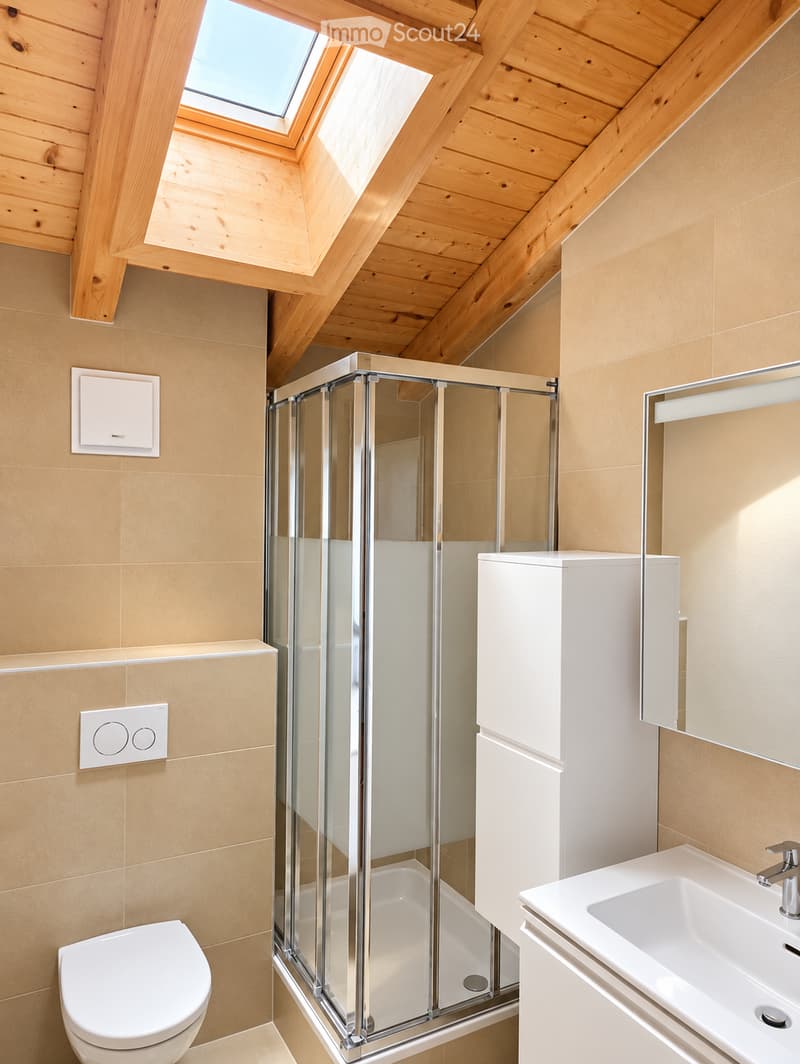 Modern bathroom with a glass-enclosed shower, toilet, sink, and mirrored cabinet. The room features light wooden beams on the ceiling and warm beige tiles on the walls.