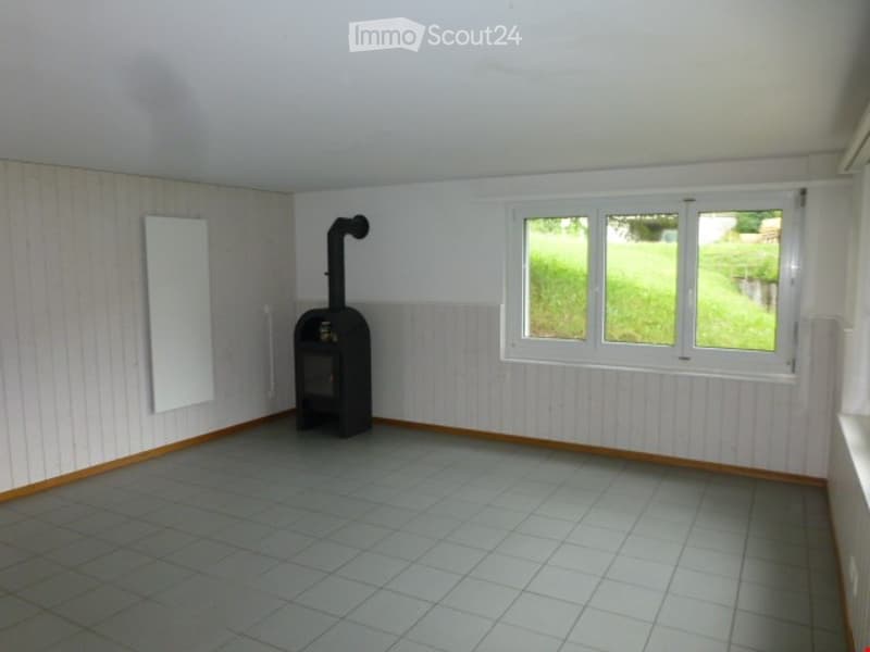 Empty room with tiled floor, white walls, and a black wood-burning stove with a chimney. There are two windows with white frames and a whiteboard on the wall.