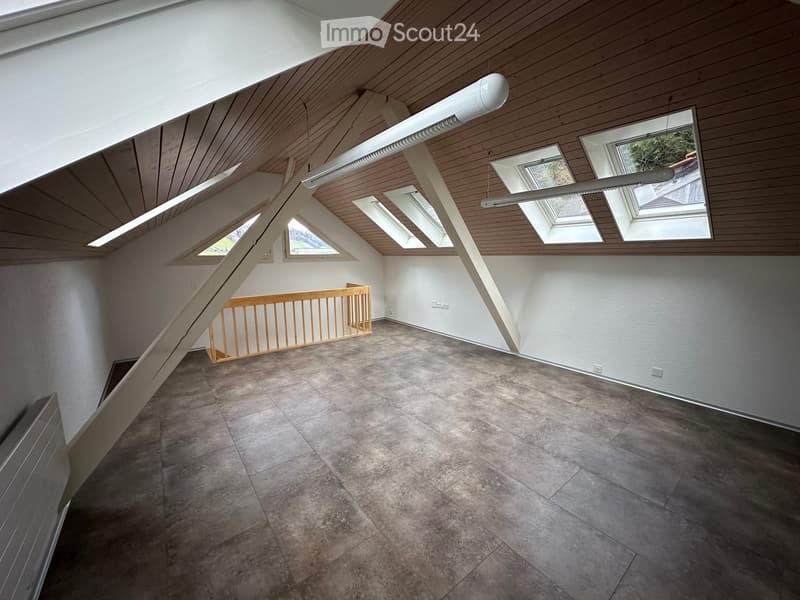 Empty attic space with wooden ceiling, skylights, and a staircase leading down. The floor is concrete, and the walls are white.