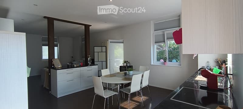 Modern kitchen with white cabinets, a dining area, and a sink. The space features a round dining table with four white chairs, a coffee maker, and various kitchen items on the counter.