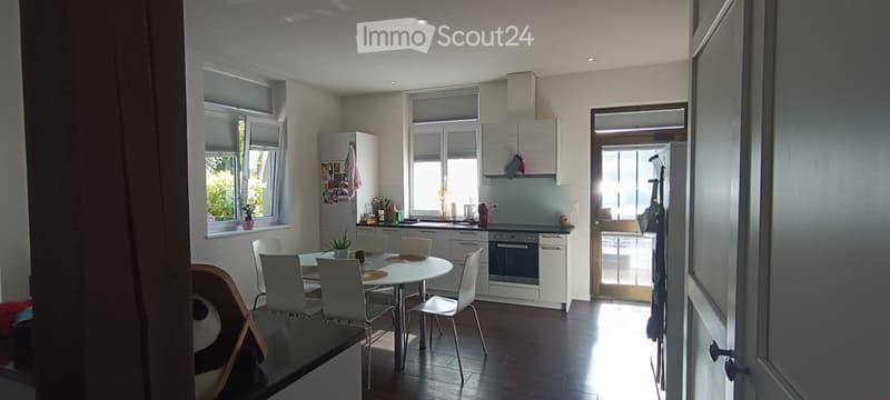 Bright, modern kitchen and dining area with white cabinets, stainless steel appliances, a round dining table with six chairs, and large windows letting in natural light.