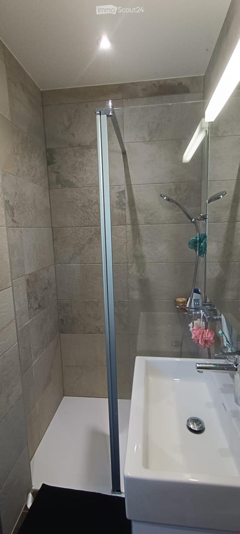Modern bathroom with a white sink, chrome faucet, and a glass-enclosed shower area with a modern showerhead. The walls are tiled in a neutral tone, and the floor is white.