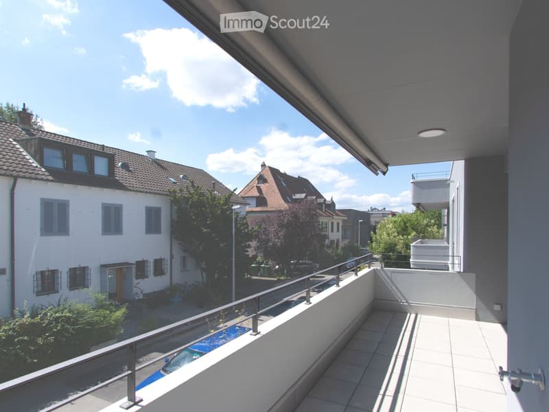 Balcony with tiled floor, metal railing, overlooking a residential street with houses, trees, and parked cars.