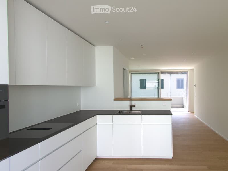 Modern kitchen with white cabinets, black countertops, and a sleek sink area. The space features recessed lighting and a wooden floor.
