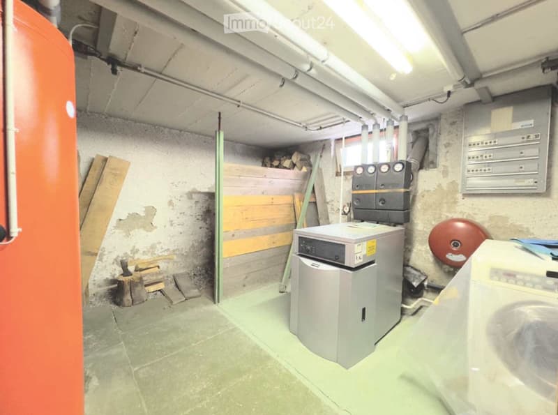 Utility room with a washing machine, heating unit, wood pile, and electrical panel.