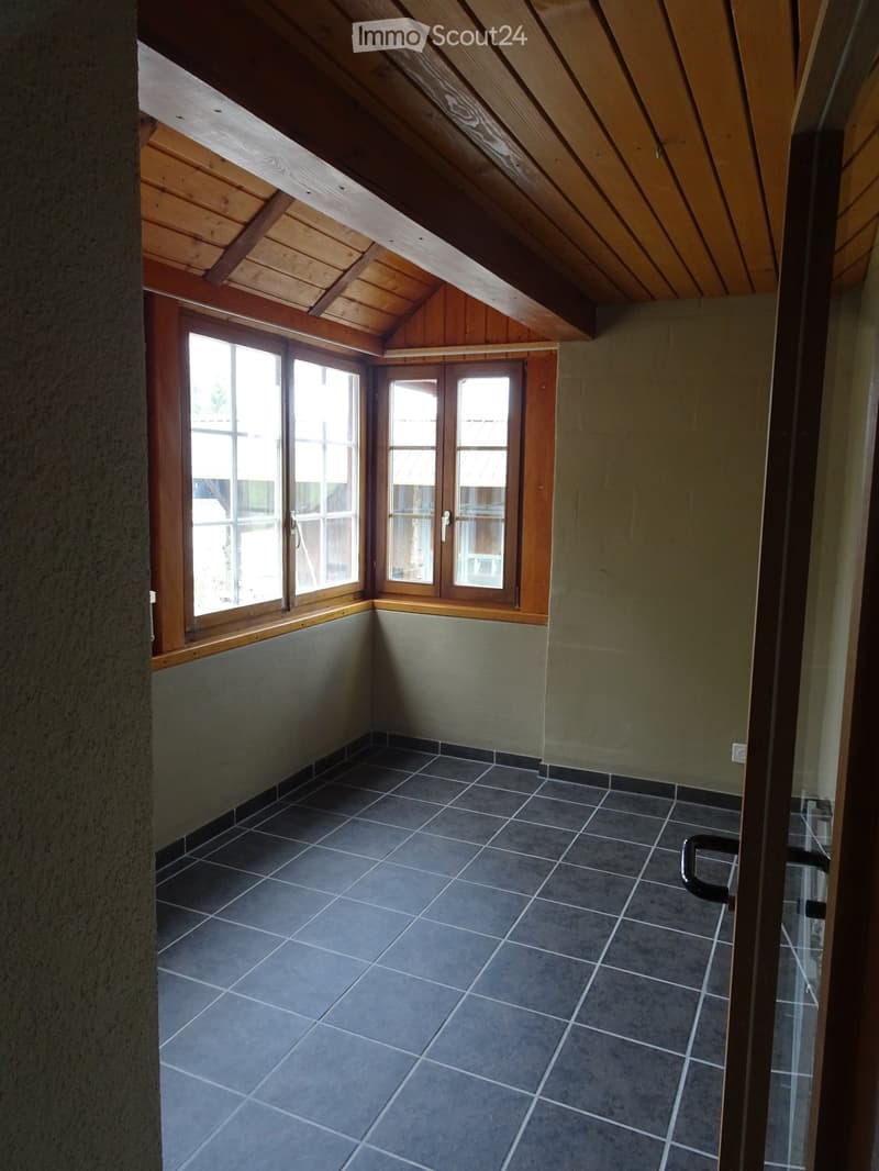 Empty attic space with wooden slanted ceilings, grey tiled floor, and large windows with wooden frames.