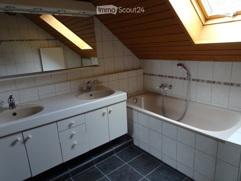 Bathroom with two sinks, a bathtub, and a large mirror above the sinks. The room features wooden slanted ceilings and skylights.