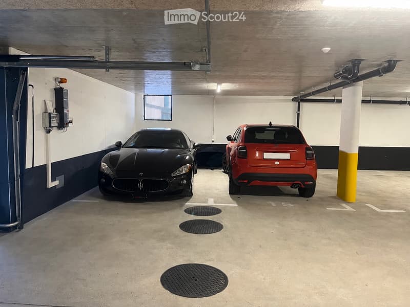 Underground parking area with two cars parked, concrete floor, white and dark blue walls, wooden ceiling, and a pillar.