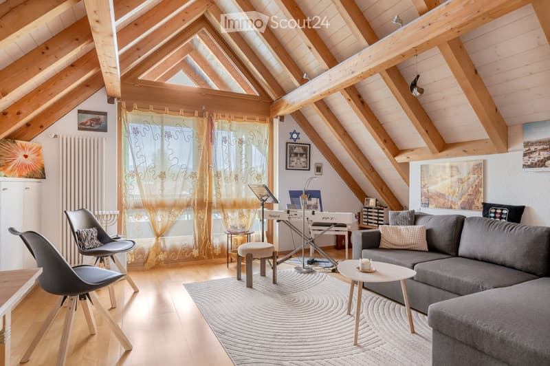 Cozy attic living room with wooden beams, exposed ceiling, large windows with sheer curtains, grey sofa, coffee table, modern chair, piano, and artwork on walls.