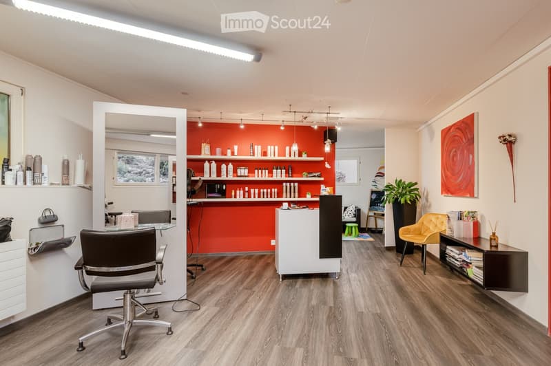 Modern, well-lit salon with wooden flooring, white and orange decor, multiple chairs, shelves with hair products, a reception desk, and a yellow accent chair.