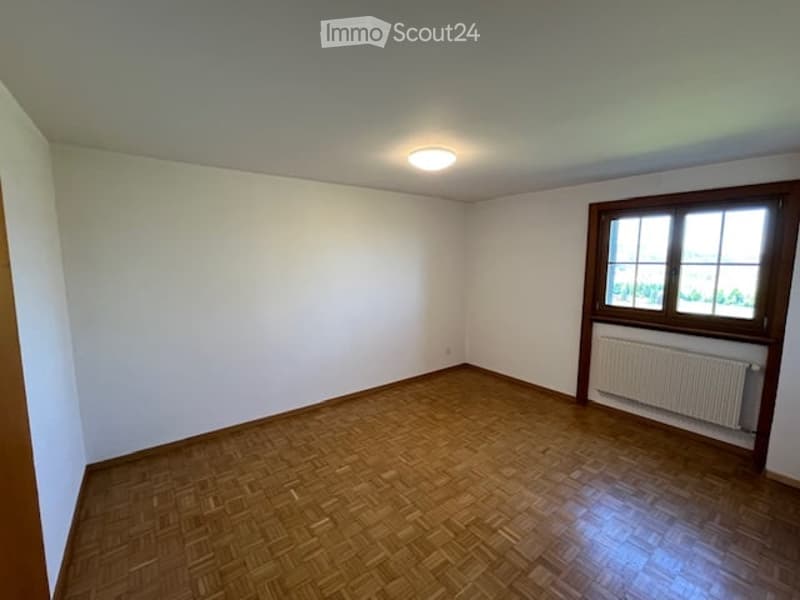 Empty room with wooden flooring, white walls, a single window with wooden frame, and a radiator below the window.