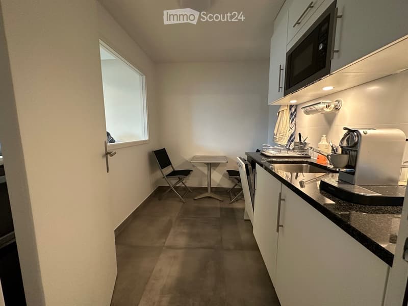 Compact kitchen area with white cabinets, microwave, sink, coffee machine, small table, and chairs.