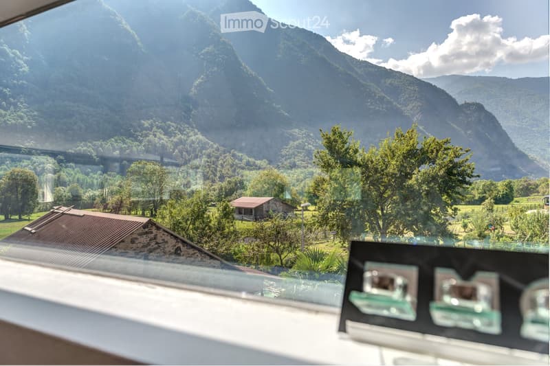 Balcony with expansive mountain view, surrounded by trees and a small rustic building in the distance.