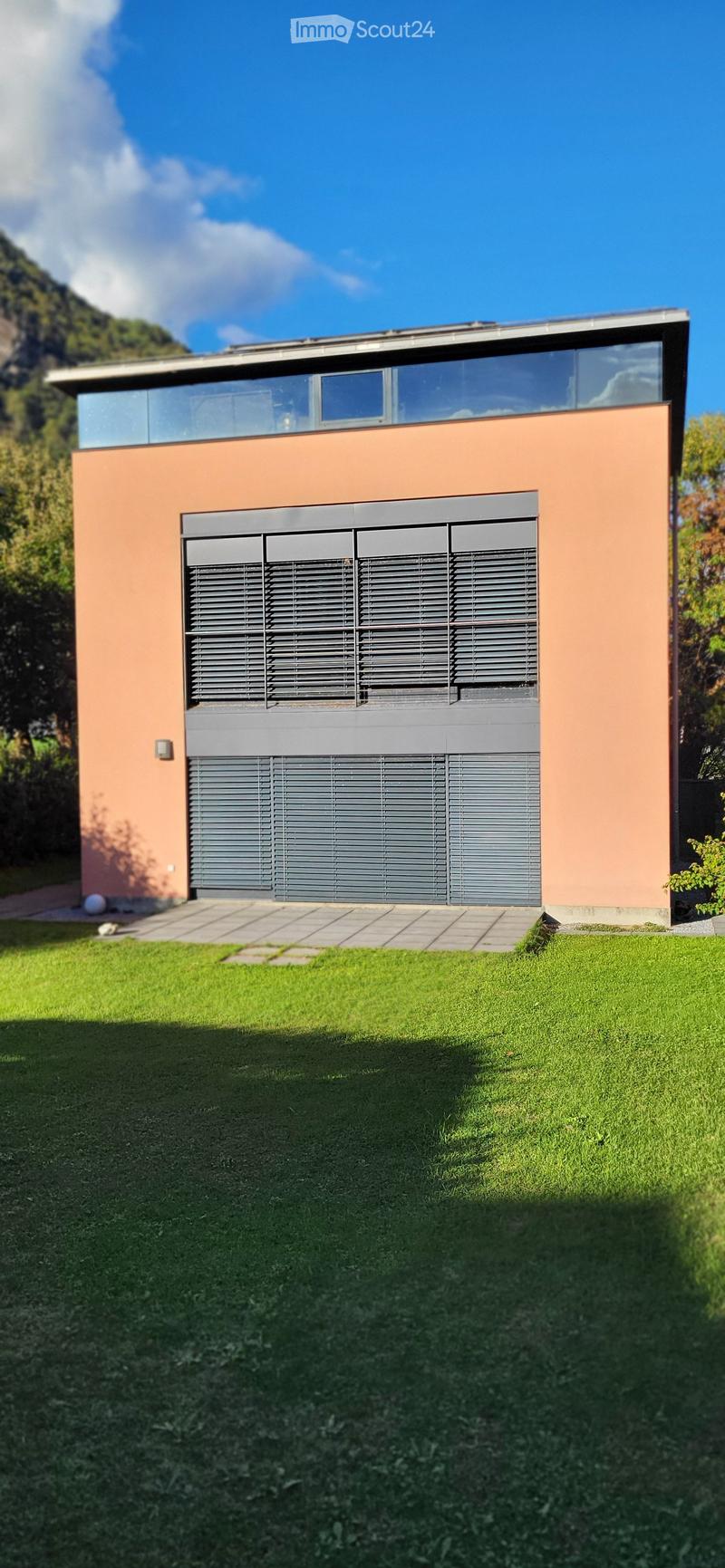 Modern two-story house with peach-colored walls, large windows, and a garage with horizontal slatted doors.