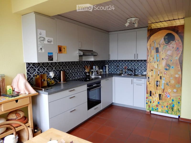 Modern kitchen with white cabinets, dark backsplash, and stainless steel appliances. Includes a sink, oven, refrigerator, and a small table with chairs.