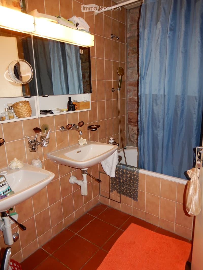 Bathroom with two sinks, a bathtub, a mirror, and a shower curtain. The room features tiled walls and a tiled floor, with various toiletries and a wicker basket on the shelves.