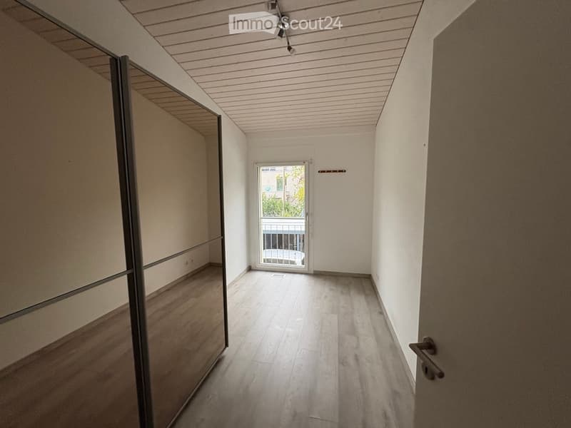 Empty hallway with light wooden flooring, white walls, and a large glass door leading to a balcony area.