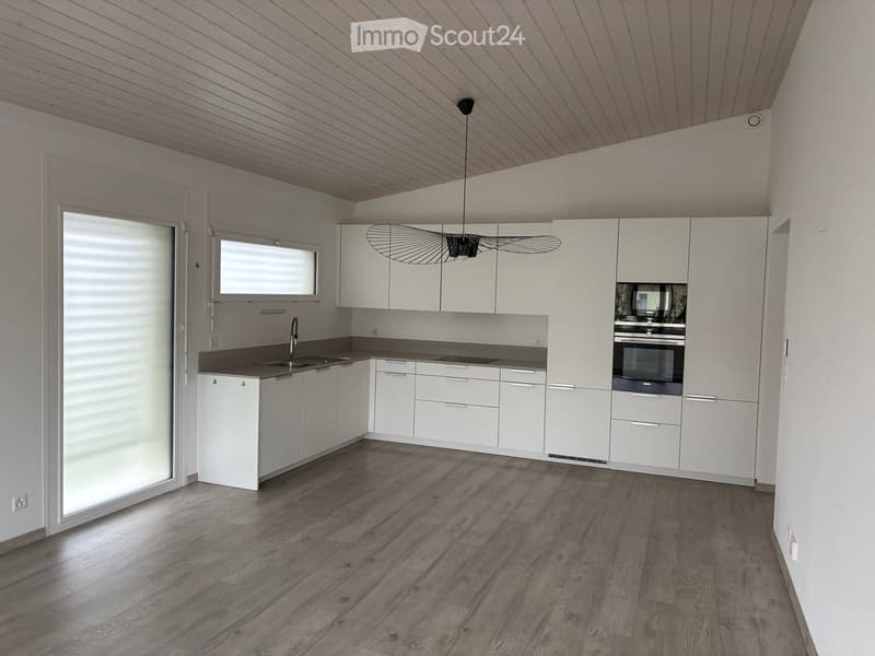 Modern kitchen with white cabinets, dark countertops, and a wooden floor. Features a sink, faucet, and built-in oven.