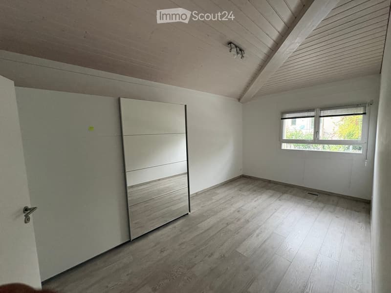 Empty room with wooden flooring, white walls, and a large window with blinds. Features a built-in wardrobe with mirrored doors and a small closet.
