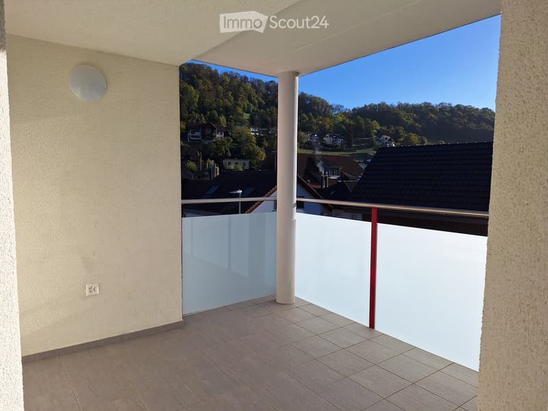 Balcony with tiled floor, white glass balustrade, and scenic view of a town and forested hills.