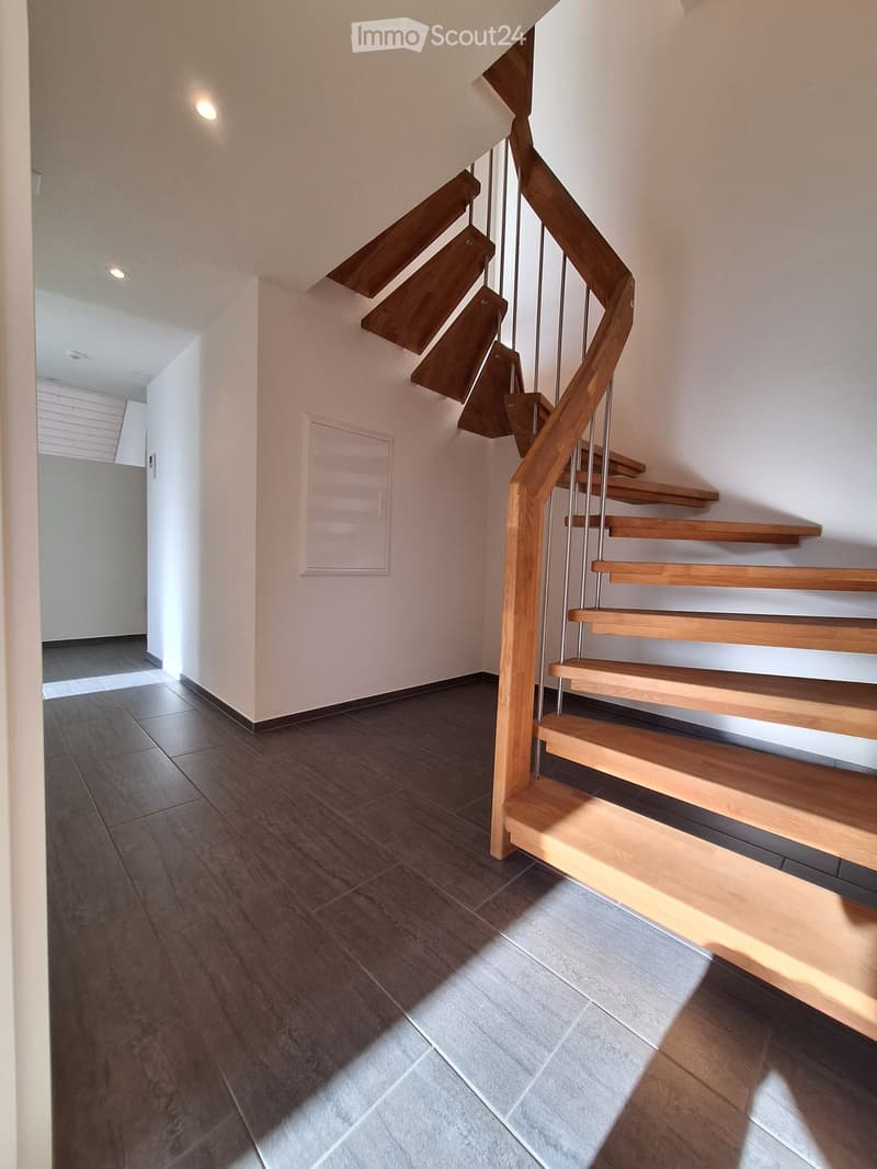 Modern hallway with wooden staircase featuring a metal railing, dark tiled floor, and recessed lighting.