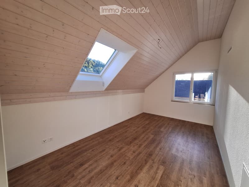 Empty attic room with wooden walls and ceiling, skylight window, and wooden flooring.