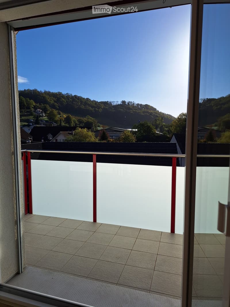 Balcony with tiled floor, glass railing, and scenic view of a town and hills under a clear blue sky.
