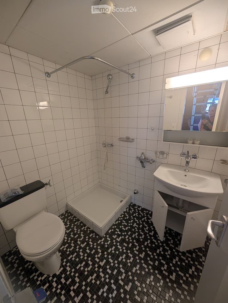 Modern bathroom with white tiled walls, black and white checkered floor, toilet, bathtub, sink, mirror, and showerhead.