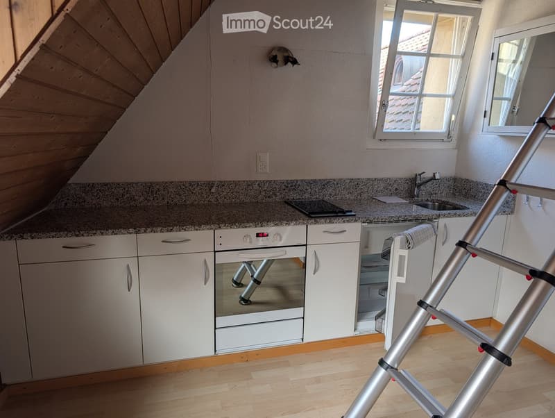 Modern kitchen with white cabinets, granite countertop, stainless steel sink, and built-in oven. Wooden floor and large window.