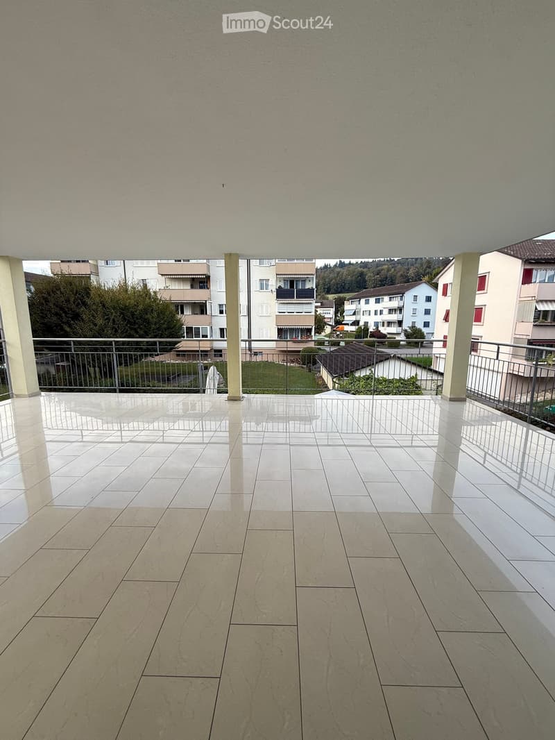 Balcony with tiled floor, metal railing, and view of surrounding buildings and greenery.