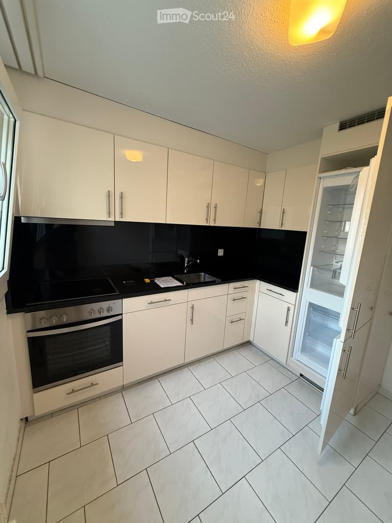 Modern kitchen with white cabinets, a stainless steel oven, a refrigerator, and a sink, featuring a black backsplash and tiled flooring.