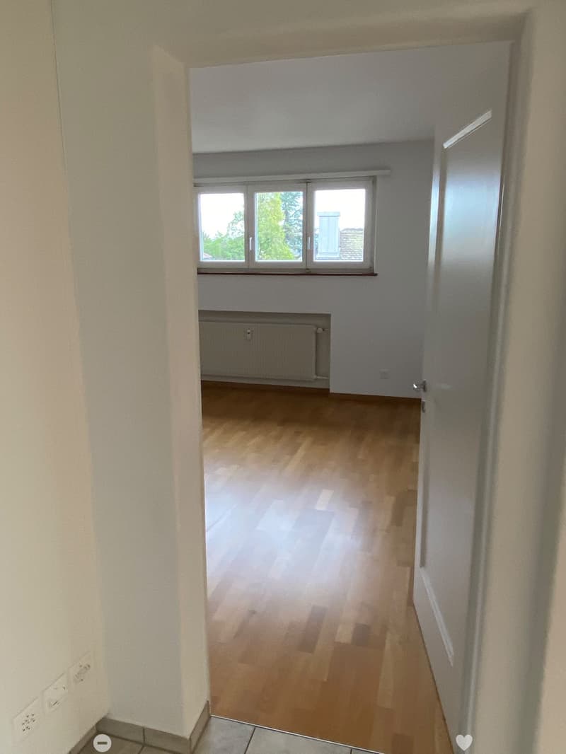 Empty hallway with wooden flooring, white walls, and a window at the end. No furniture or equipment present.