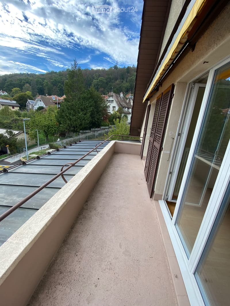Balcony with concrete floor, metal railing, and scenic view of a residential area with trees and houses.